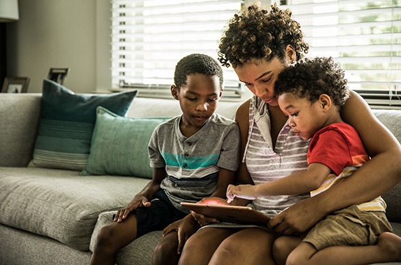 Single mother using tablet with young sons on couch